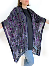Load image into Gallery viewer, women modeling devoré or burnout velvet kimono jacket holding up arms to show kimono style over black top and jeans.  The duster style jacket is black sheer chiffon background with an all over pattern of willow branches with purple accents
