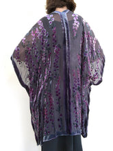 Load image into Gallery viewer, women modeling devoré or burnout velvet kimono jacket showing the back. Long duster style over black jeans. The duster style jacket is black sheer chiffon background with an all over pattern of willow branches with purple accents