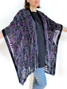 women modeling devoré or burnout velvet kimono jacket holding up arms to show kimono style over black top and jeans.  The duster style jacket is black sheer chiffon background with an all over pattern of willow branches with purple accents