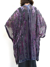 Load image into Gallery viewer, women modeling devoré or burnout velvet kimono jacket showing the back. Long duster style over black jeans. The duster style jacket is black sheer chiffon background with an all over pattern of willow branches with purple accents
