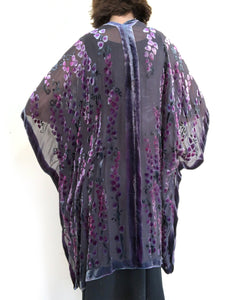 women modeling devoré or burnout velvet kimono jacket showing the back. Long duster style over black jeans. The duster style jacket is black sheer chiffon background with an all over pattern of willow branches with purple accents